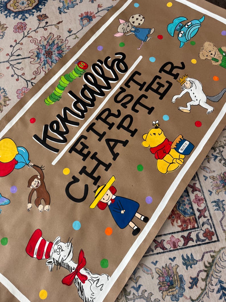 May include: A brown paper banner with the text "Kendall's FIRST CHAPTER" and colorful illustrations of storybook characters. The banner features a white border and colorful polka dots.