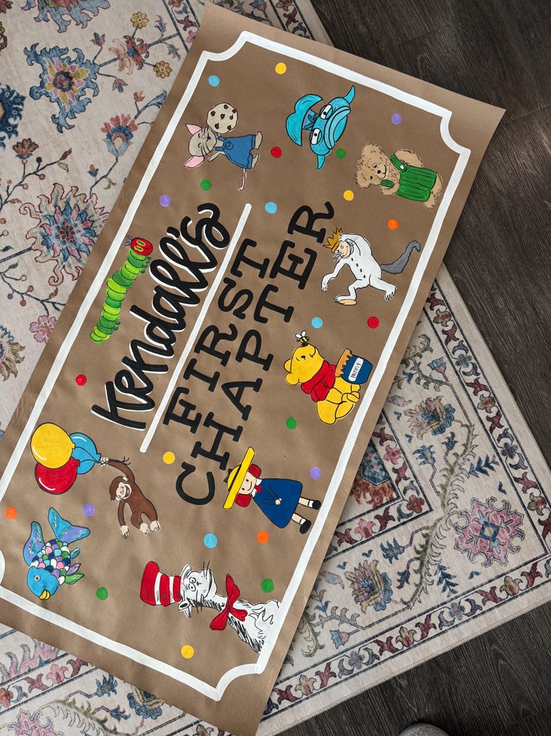 May include: A brown paper banner with the text "Kendall's FIRST CHAPTER" in black and white, surrounded by colorful cartoon characters. The banner is bordered with a white frame and features illustrations of a caterpillar, Winnie the Pooh, and other storybook characters.