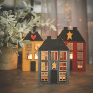 May include: Three wooden houses with lit windows, one yellow, one red, and one blue. Each house has a star or heart on the front.