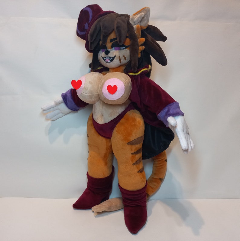 May include: A plush toy of a cat-like creature wearing a purple and black robe with a pointed hat. The toy has brown fur, a long tail, and is wearing red boots.