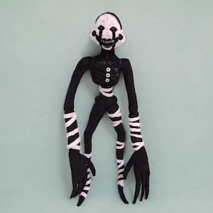 Puede incluir: Muñeco de peluche hecho a mano de un personaje con cabeza blanca y rasgos faciales negros. El muñeco tiene un cuerpo negro con detalles blancos, incluyendo brazos y piernas a rayas. Las manos del muñeco son negras.