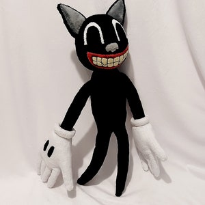 May include: A black cartoon cat plush toy with a wide, toothy grin and large, white eyes. The toy has white gloves and is standing on a white surface.