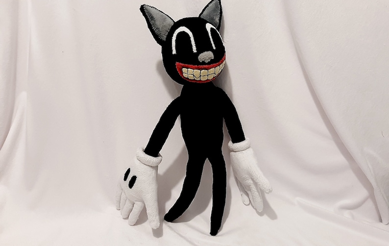 May include: A black cartoon cat plush toy with a wide, toothy grin and large, white eyes. The toy has white gloves and is standing on a white surface.