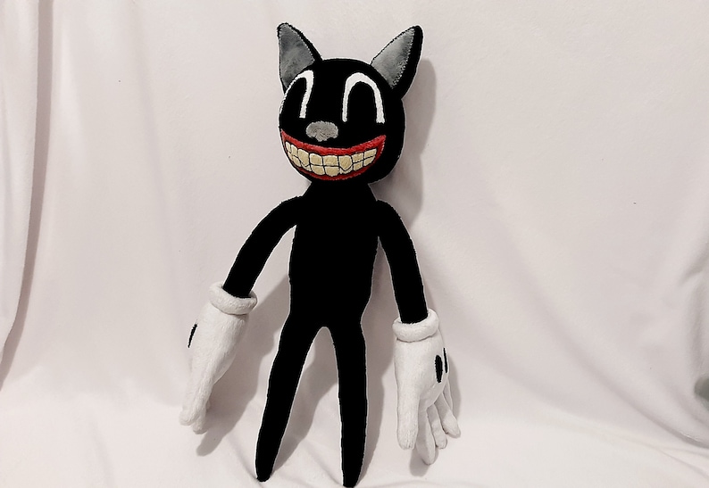 May include: A black cartoon cat plush toy with a wide, toothy grin. The cat has large, white eyes and red lips. The cat is wearing white gloves and has a long, thin body.