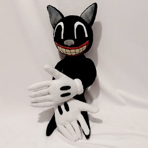 May include: A black cartoon cat plush toy with a wide, toothy grin. The toy has white gloves and is sitting on a white surface.