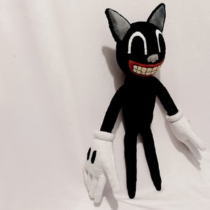 May include: A black cartoon cat plush toy with a wide, toothy grin. The toy has white gloves and large, white eyes. The toy is standing on a white surface.