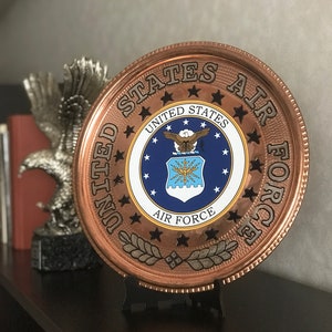 May include: A copper-colored round plaque with the words "United States Air Force" and the Air Force emblem in the center. The plaque is on a black stand.