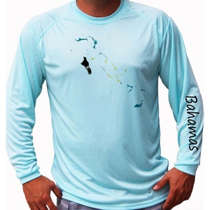 May include: A light blue long-sleeved shirt with a graphic of the Bahamas islands. The shirt has the word "Bahamas" printed on the right sleeve.