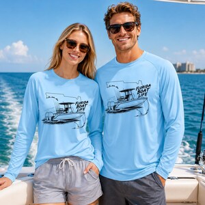 May include: Light blue long-sleeve shirts featuring a black graphic print of a boat with fishing rods and the text Florida Boat Life. The shirts have a crew neckline and are made of a lightweight material, suitable for outdoor activities on the water.