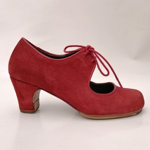 May include: Red suede heeled shoe with a rounded toe and lace-up closure. The shoe features a mid-height heel and a cutout design on the side. The shoe's heel is approximately 2 inches (5 cm) high.