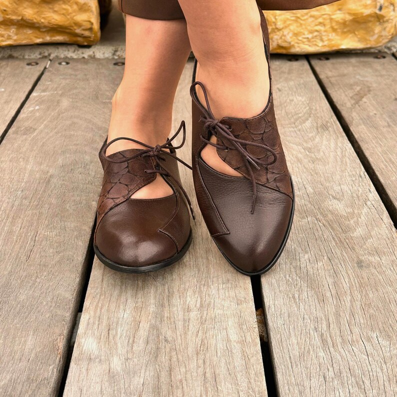 May include: Brown leather lace-up shoes with cut-out detailing. The shoes have a pointed toe and a low heel.