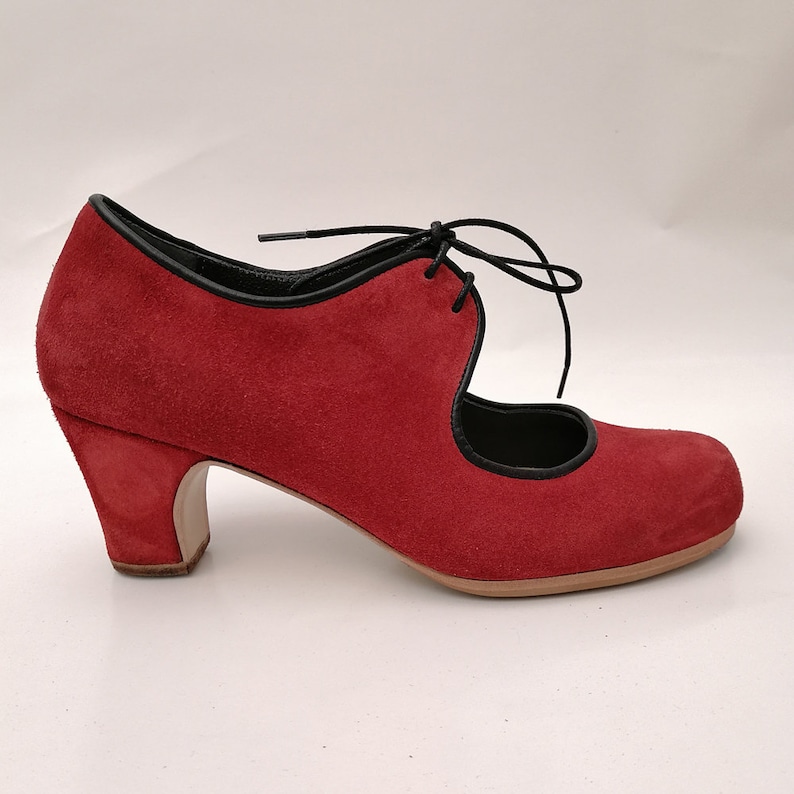May include: A red suede shoe with a rounded toe and a mid-height heel. The shoe features black trim along the edges and a lace-up closure. The heel measures approximately 2.5 inches.