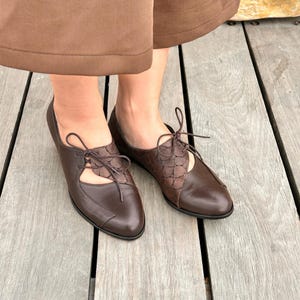 May include: Brown leather lace-up shoes with cut-out detailing. The shoes have a pointed toe and a low heel.