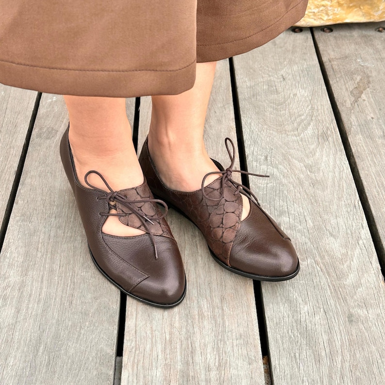 May include: Brown leather lace-up shoes with cut-out detailing. The shoes have a pointed toe and a low heel.