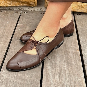 May include: Brown leather lace-up shoes with a cut-out detail on the side. The shoes have a rounded toe and a low heel.