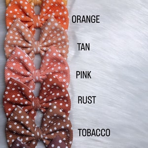Könnte beinhalten: Acht gepunktete Haarbänder in verschiedenen Farben, darunter Grün, Gelb, Orange, Braun, Rosa, Rost, Tabak und Schokolade.