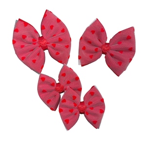 May include: Four red hair bows with white mesh and small red hearts printed on the fabric. The bows are tied in a knot in the centre.
