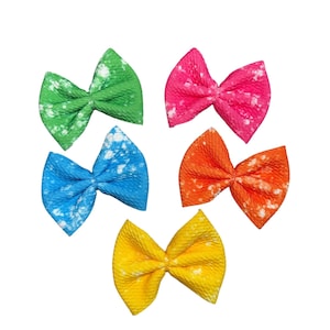 May include: Six colorful hair bows with a white splatter paint design. The bows are in shades of green, pink, blue, orange, and yellow.