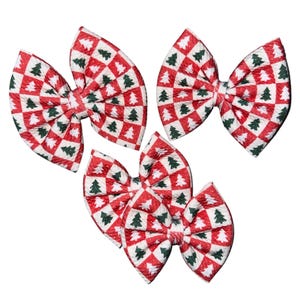 Puede incluir: Cinco lazos para el pelo con un diseño de árbol de Navidad. Los lazos presentan un patrón de cuadros rojos y blancos con árboles de Navidad verdes. Cada lazo tiene un nudo central y extremos en bucle, dispuestos en un grupo sobre un fondo blanco.