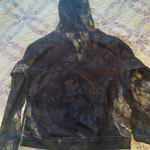 May include: A black hooded sweatshirt with a camouflage pattern. The hoodie has a drawstring and a zipper closure.