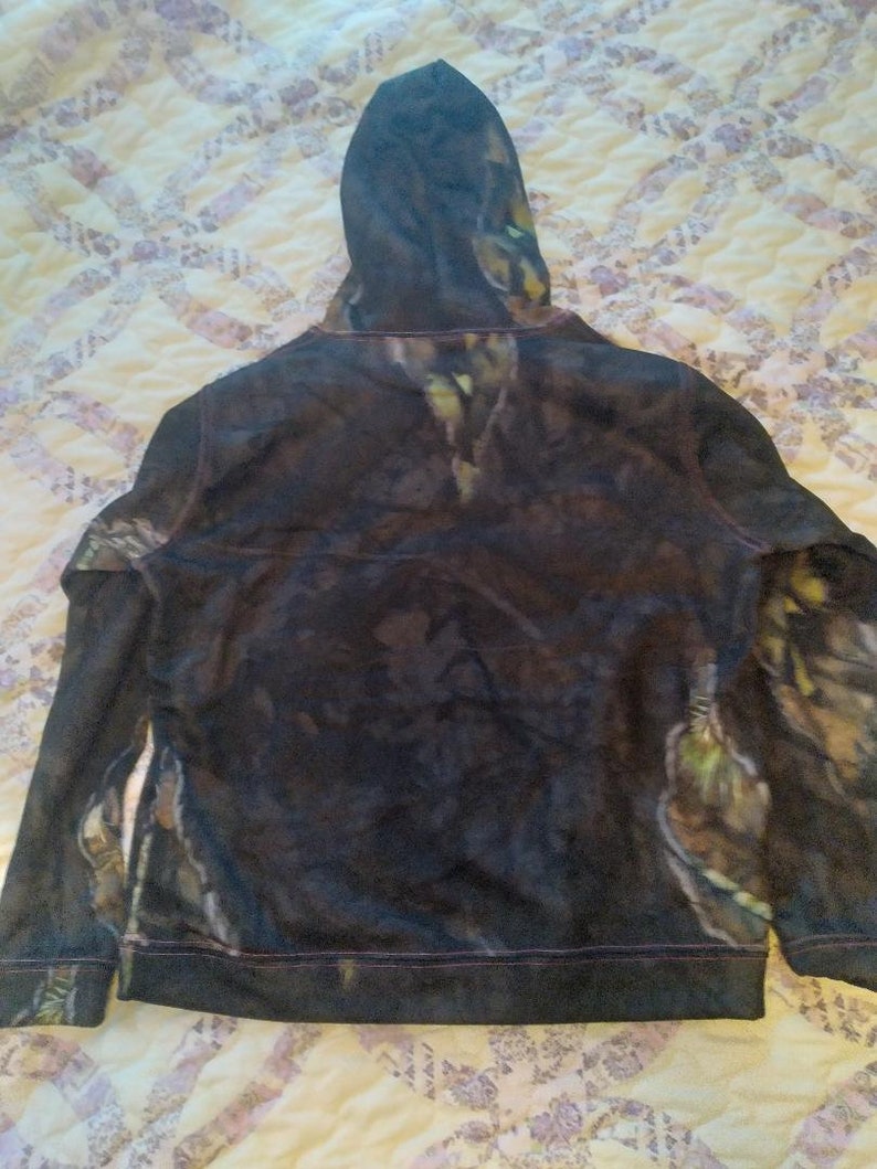May include: A black hooded sweatshirt with a camouflage pattern. The hoodie has a drawstring and a zipper closure.