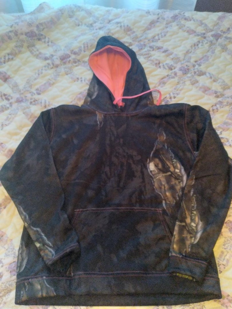May include: A black and brown camouflage hoodie with a pink lining and a drawstring hood.