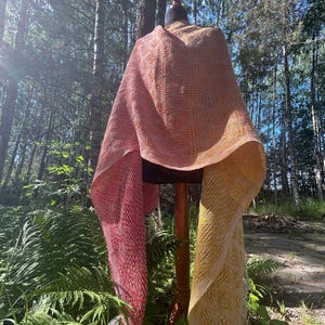Könnte beinhalten: Ein gewebter Schal mit einem Farbverlauf von tiefem Rot zu Orange und Gelb, mit einem strukturierten Rautenmuster und weißen Fransen an den Enden. Der Text ZACŁOD SŁONCA und STREFATKANIA.ORG ist auf dem Bild aufgedruckt.
