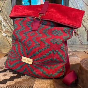 Puede incluir: Una mochila estampada en rojo y verde con cierre enrollable. La bolsa presenta una correa y detalles en burdeos, con un cierre dorado. La parte superior es de un material rojo afelpado. El texto "Strefa Tkania" es visible.