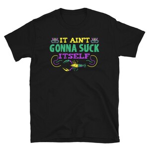 May include: Black t-shirt with the phrase "IT AIN'T GONNA SUCK ITSELF" in green, yellow, and purple. The design includes a crawfish and Mardi Gras mask graphics. A fun and festive tee.