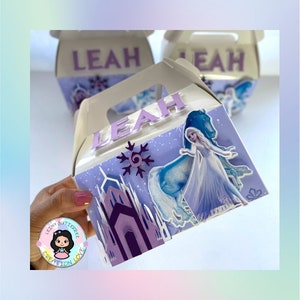 May include: A purple and blue Frozen themed party favor box with a picture of Elsa and her horse. The box has a handle and says "LEAH" on the front.