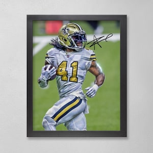 Peut inclure: Impression encadrée d'un joueur de football américain en uniforme or et blanc, portant le numéro 41, courant avec le ballon. Le joueur porte un casque et des gants dorés. L'image est sur fond vert et comprend un autographe.