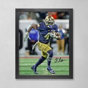 May include: Framed action shot of a football player in a navy blue and gold uniform, number 4, running with the ball. The player wears a gold helmet and gloves. The image is set on a green field with a blurred background.