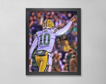 May include: Framed print of a football player in a green and gold uniform, number 10, with the name "LOVE" on the helmet. The player is pointing upwards, with a signature and the number 10 visible. The background shows a blurred crowd.