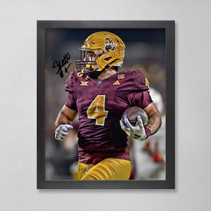 May include: Framed print of a football player in a maroon and gold uniform, helmet, and pads, holding a football. The player is running, with the number 4 on the jersey. The frame is black, and the background is blurred.
