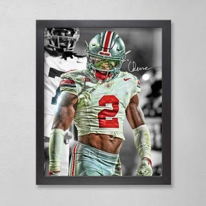 May include: Framed print featuring a football player in a white and red uniform with the number 2. The player is wearing a helmet with a silver and red stripe. A black and white image of another player is in the background.