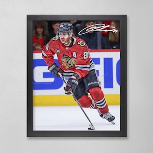 Op de afbeelding: Ingelijste print van een hockeyspeler in een rood en zwart Chicago Blackhawks-shirt, nummer 81. De speler schaatst op het ijs met een hockeystick. De lijst is zwart en de achtergrond toont toeschouwers.