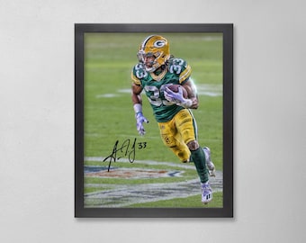 May include: Framed print of a football player in a green and gold uniform, running with the ball. The player is wearing a helmet and gloves. The image is signed with the number 33.