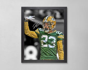 May include: Framed print of a football player in a green and gold uniform, number 23, with a gold helmet. The player is raising his hand in a gesture, with a black and white background. The frame is black.