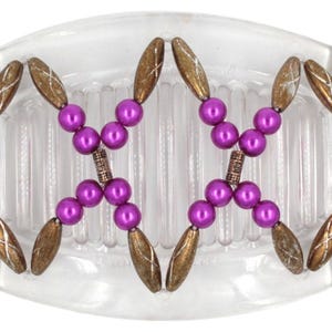 May include: A clear plastic hair comb with a decorative design of purple beads and gold-colored metal accents.