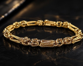 May include: A gold-toned bracelet featuring a complex, repeating chain link design. The structure alternates between smooth, rounded circular links and elongated, textured rectangular links with a cross-hatched pattern, finished with a secure clasp.