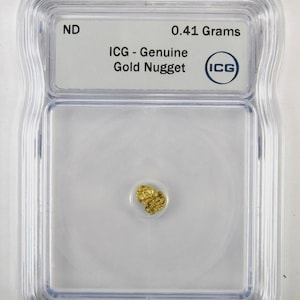 Peut inclure: Une petite pépite d'or métallique texturée enfermée dans un étui de protection rectangulaire en plastique transparent. L'étiquette à l'intérieur indique ND, 0.41 Grams, ICG - Genuine Gold Nugget, avec le logo ICG dans un cercle bleu.