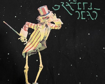 May include: Black t-shirt with a white skeleton wearing a red, white, and blue hat and a striped jacket. The skeleton is holding a cane and is standing on a black background with white dots. The text "THE GRATEFUL DEAD" is written in green on the shirt.