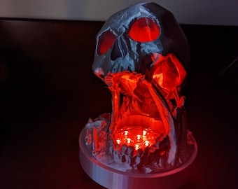 May include: A white 3D printed skull with a red light emanating from the mouth. The skull is sitting on a white base with a circular light source in the center.