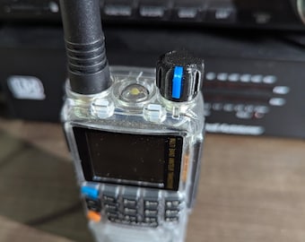 Pode incluir: Um rádio portátil transparente com uma antena preta e um botão preto com uma faixa azul. O rádio tem uma tela pequena e um teclado. O texto "Radio NOT included" é visível no fundo.