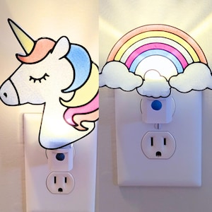 May include: Two night lights, one with a unicorn design and the other with a rainbow design. Both are plugged into electrical outlets.