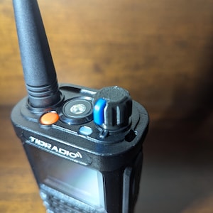 May include: A black two-way radio with a black antenna, a blue and black knob, and a screen that says "TDI RADIO".