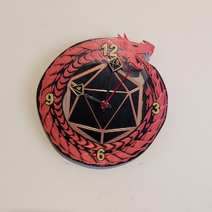 May include: A red dragon clock with a black and gold 20-sided die face. The clock face has numbers 1-12 and the die face has numbers 1-20.