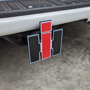 May include: A red and black International Harvester logo on a white truck hitch.
