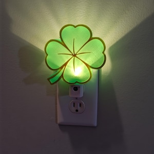 Peut inclure: Une veilleuse en forme de trèfle à quatre feuilles verte branchée sur une prise électrique.