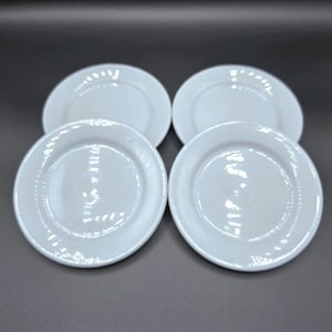 May include: Four white ceramic plates arranged in a square formation. Each plate has a slightly raised rim and a smooth, glossy surface. The plates are round and appear to be of a standard size, suitable for serving various dishes.